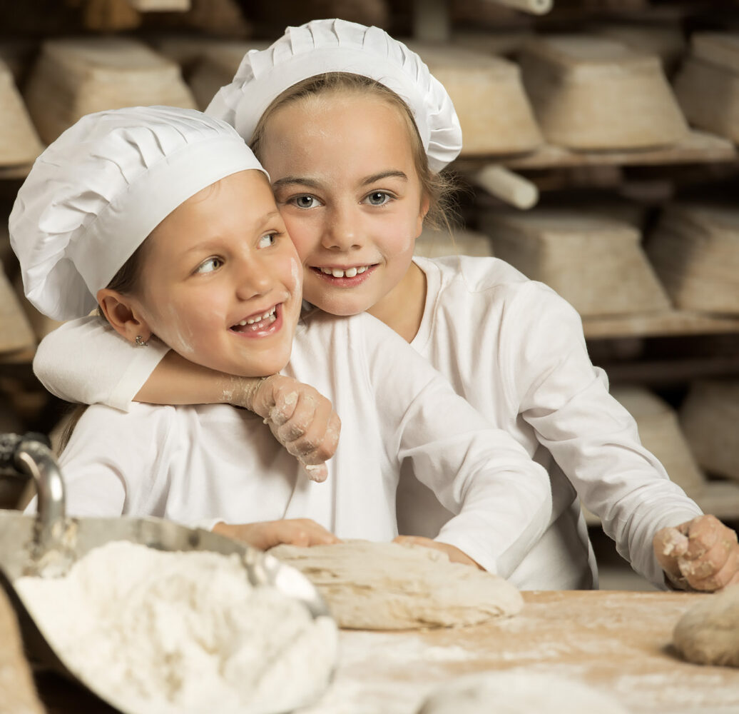 Two children in baker's hats kneading dough – people photography by Roman Kasperski