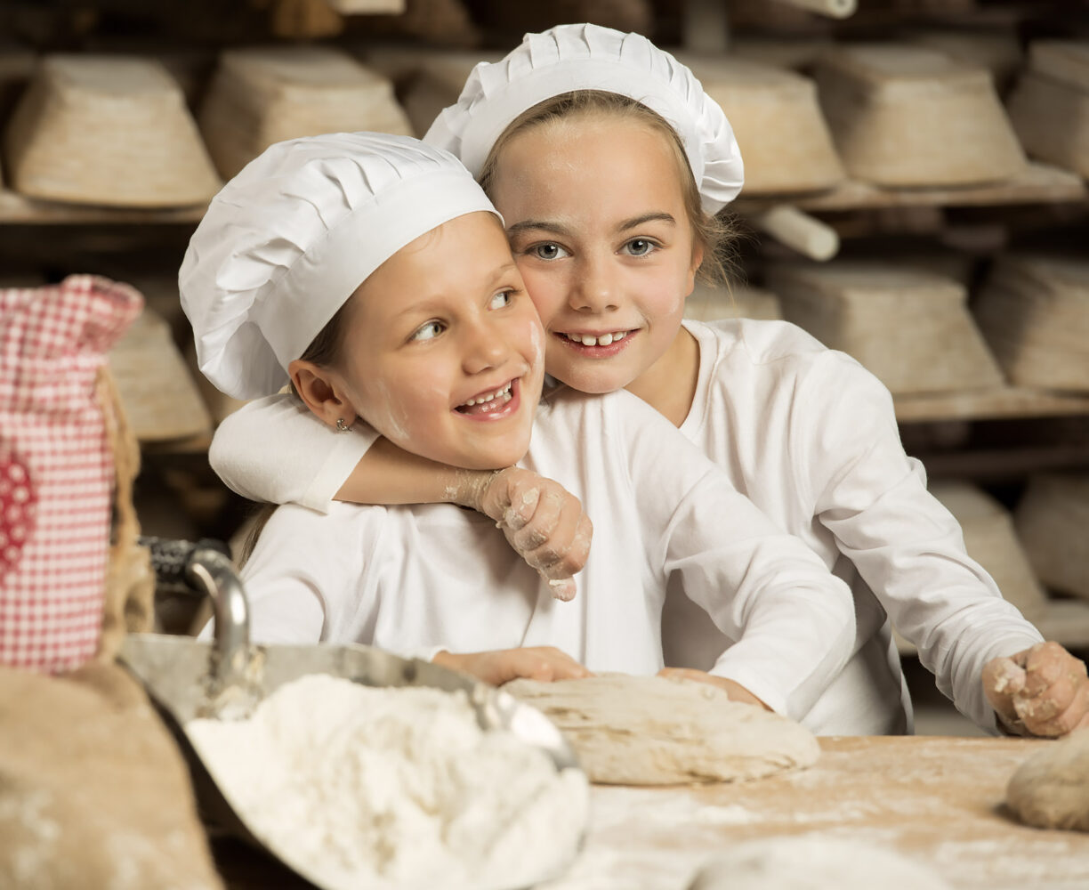 Two children in baker's hats kneading dough – people photography by Roman Kasperski